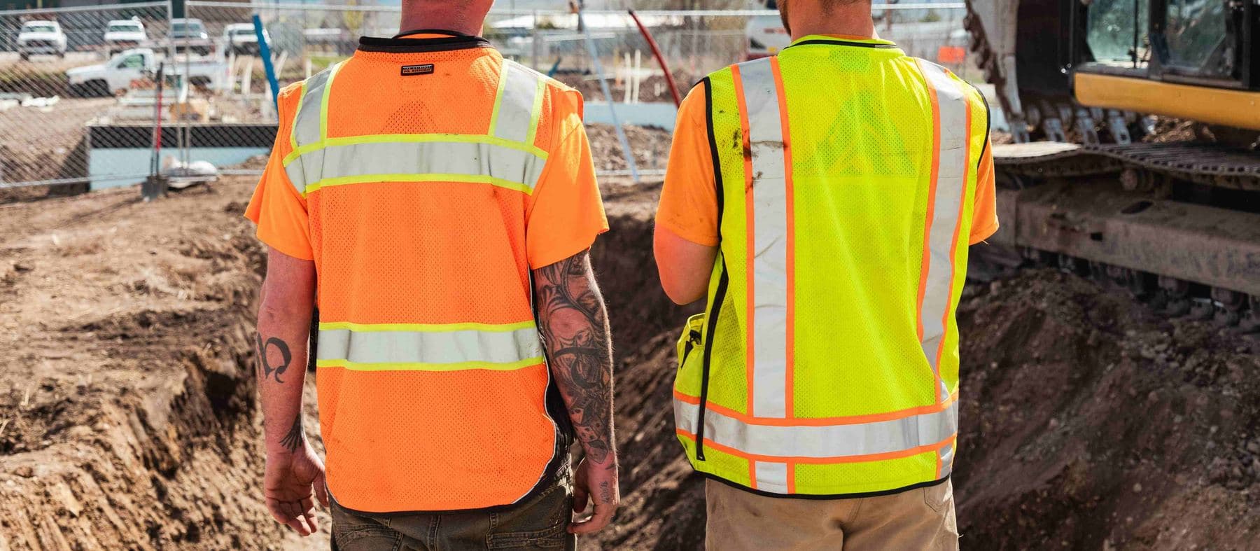 Two workers in hi-vis vests watching an excavator dig a trench