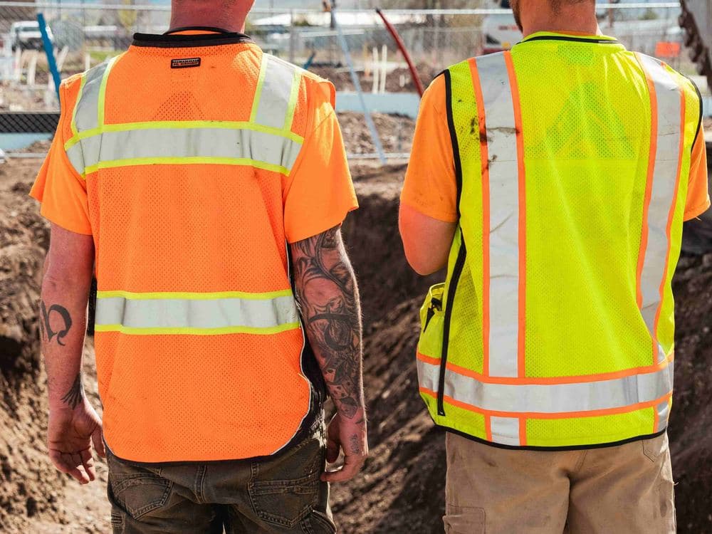 Two workers in hi-vis vests standing beside an open trench