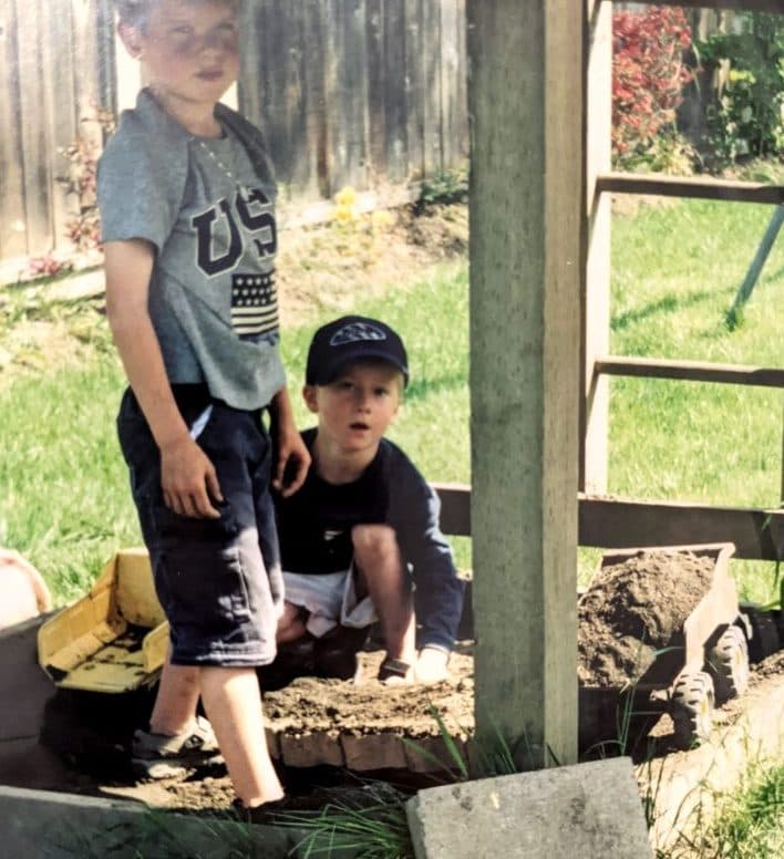 Andrew as a kid in a backyard sandbox, with a yellow toy dump truck full of dirt